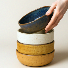 Stack of ceramic bowls with a hand lifting one, on a neutral background